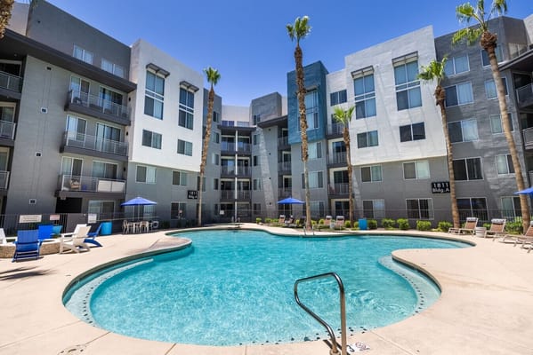 Swimming pool surrounded by palm trees and apartment buildings.