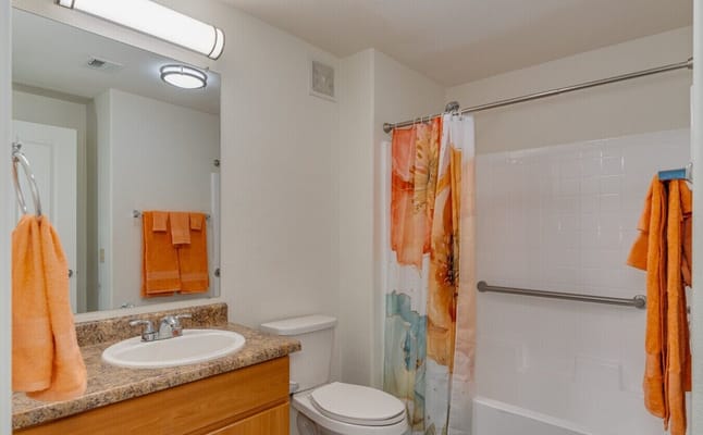 Well-lit bathroom with orange towels and floral shower curtain