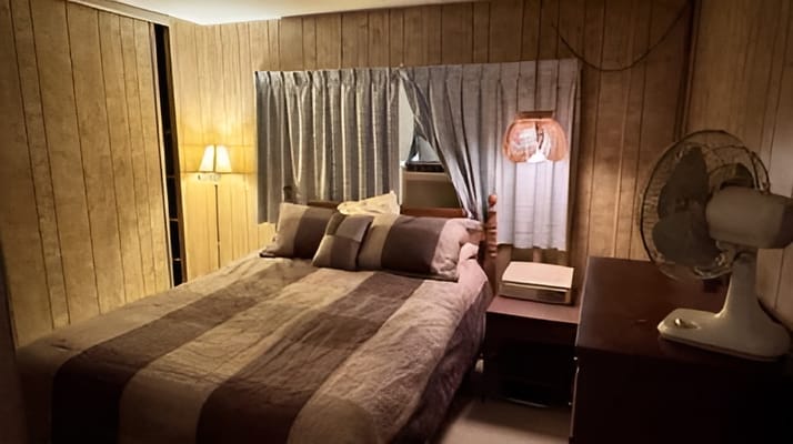 A well-furnished bedroom featuring a bed, lamp, and fan.