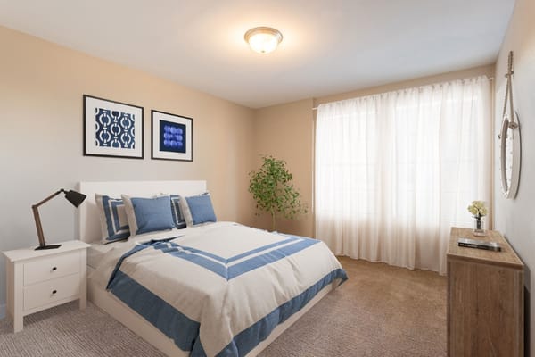 Bright bedroom with a bed, decorated with blue pillows, a lamp, and large windows