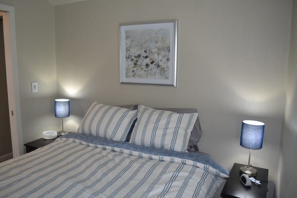 A neatly made bed with striped linens and blue lamps in a warm-toned room.