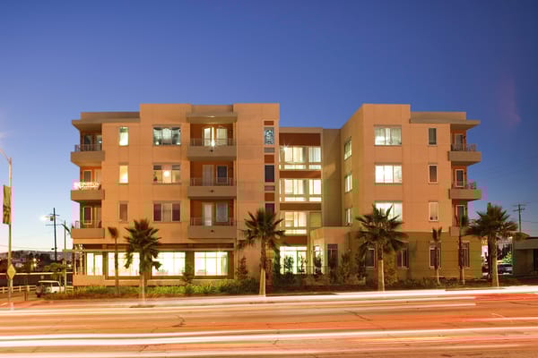 Modern senior housing facility exterior with palm trees at dusk