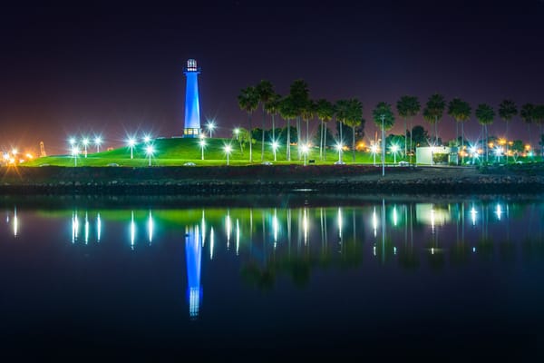 Illuminated lighthouse alongside palm trees at night
