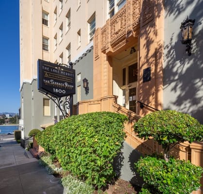 The entrance of The Lake Merritt Apartments with a sign and well-maintained greenery