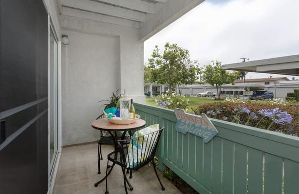 A small balcony with a round table and chairs, surrounded by greenery.