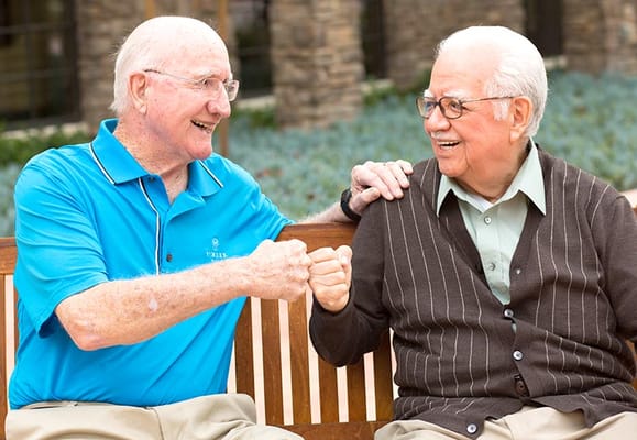Two seniors smiling and fist bumping on a bench