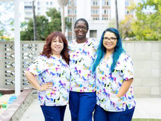 Three staff members in colorful scrubs outdoors