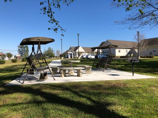 Seating area with swings and a stone table in a grassy outdoor space