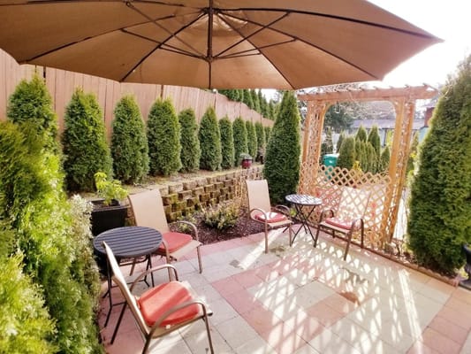 Cozy outdoor patio with chairs and sunshade surrounded by greenery.
