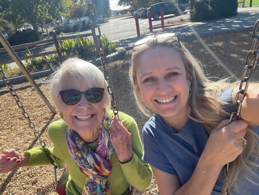 Smiling older woman and caregiver on swings in a park