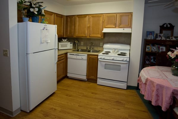 A bright kitchen with wooden cabinets, appliances, and a dining table.