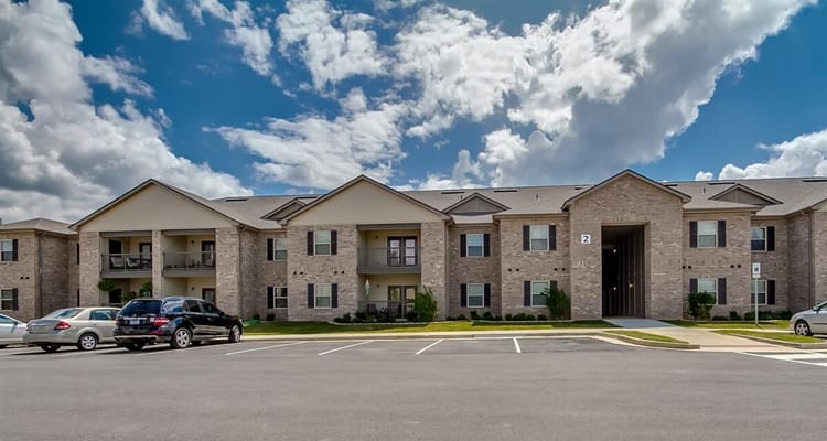 Exterior of Somerville Apartments with parked cars and a cloudy sky.