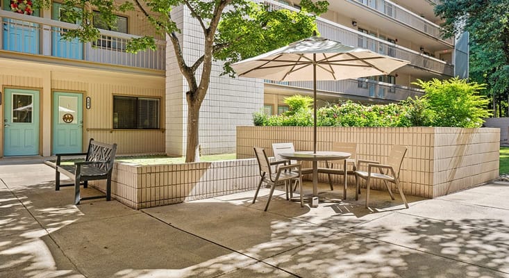 Outdoor seating area with a table and umbrella in front of an apartment building