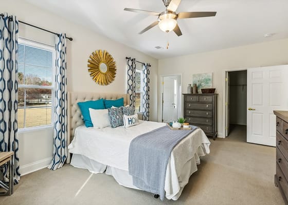 A stylish bedroom featuring a bed with blue and white accents, a dresser, and large windows.