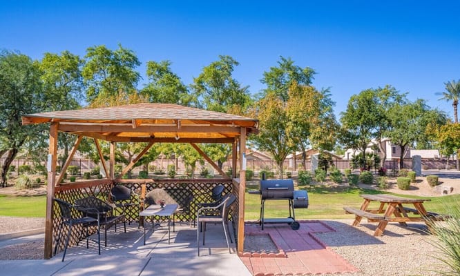 Wooden gazebo with seating area and a grill in a green outdoor space