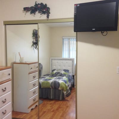 A cozy bedroom with a mirrored wardrobe, a bed, and a TV mounted on the wall.