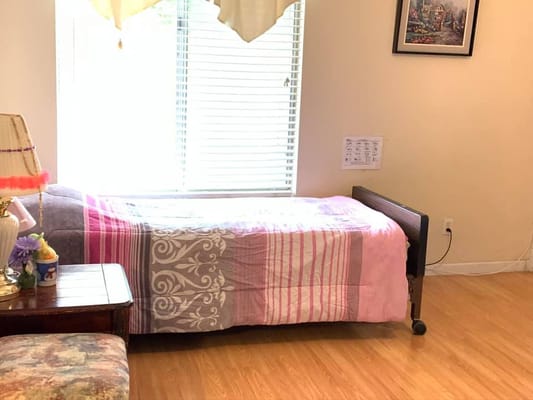 A well-lit bedroom with a bed covered in a pink and gray comforter, a bedside table, and a lamp.