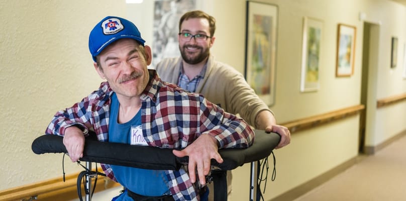 A man being assisted in a hallway by a staff member