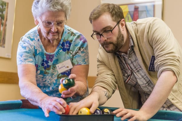 Residents and staff playing pool in an activity room
