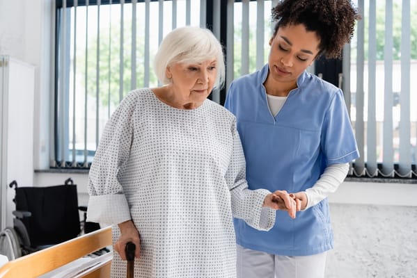 A nurse helps an elderly resident with a cane.