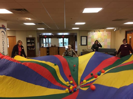 Residents participating in a colorful parachute activity indoors.