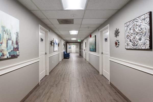 A spacious hallway with artwork and doorways in a senior living facility.