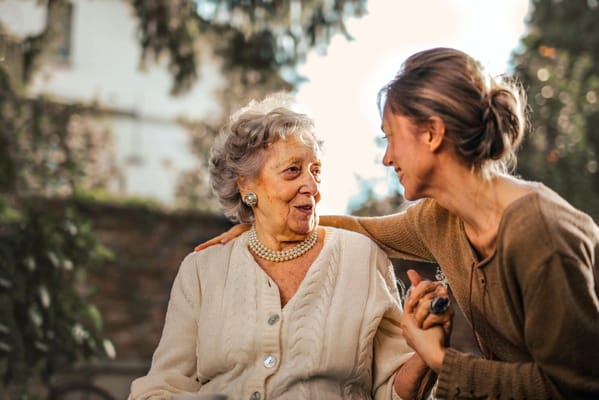 Elderly woman and caregiver smiling together outdoors