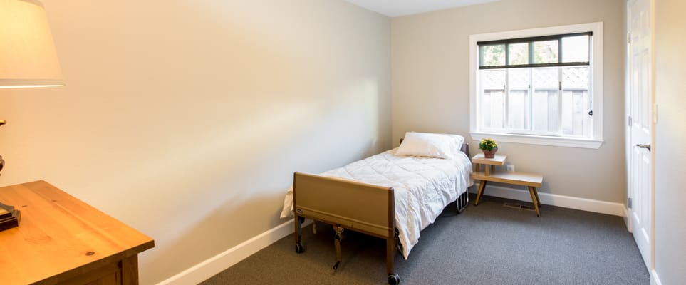 A simple, clean private resident room with a bed and side table