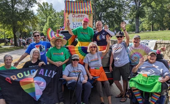A group of seniors celebrating at the Pride Parade with rainbow-themed attire and signs.