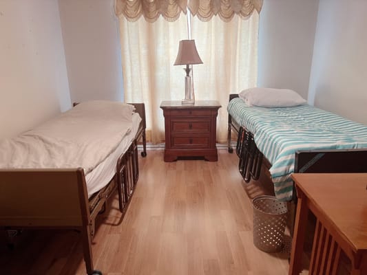 A shared bedroom with two beds, a lamp, and a small nightstand.