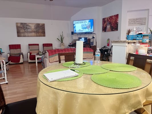 Table set with green placemats in a common area with seating and a TV.
