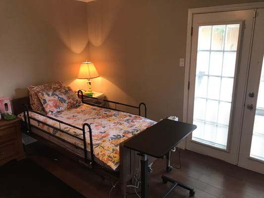 A cozy bedroom in a senior living facility with a hospital bed and nightstand.