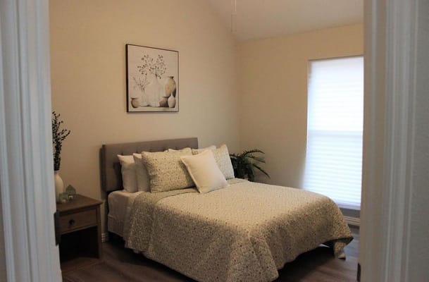 A cozy bedroom featuring a bed with floral bedding and natural light from a window.