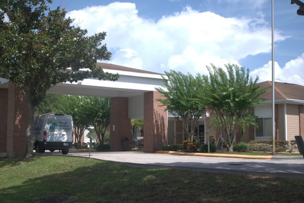 Exterior view of a senior care facility with a van and trees