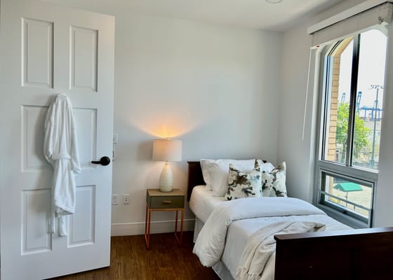 A well-lit bedroom with a bed, decorative pillows, and a bedside lamp.