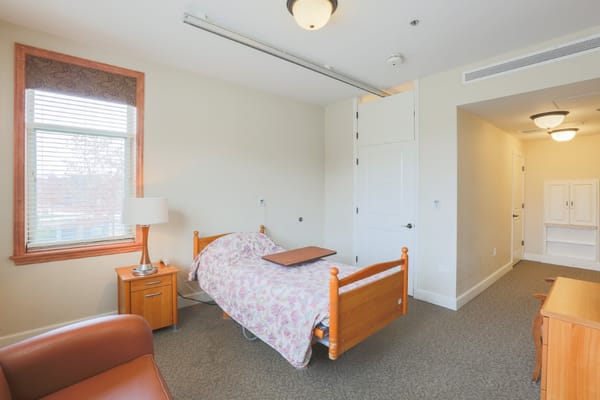 A comfortable resident room featuring a bed, bedside table, and window.