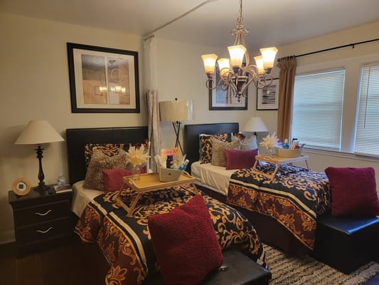 A shared bedroom in The Angel Network of Baltimore Assisted Living Facility, featuring two beds with colorful bedding and decorative pillows.