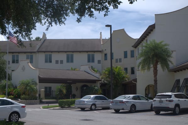 Front entrance of Arbor Terrace Citrus Park with palm trees and parked cars