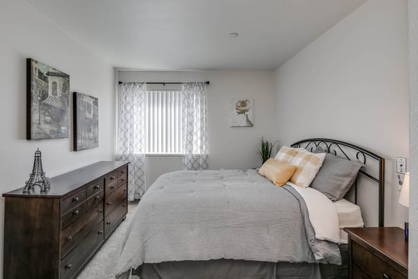 A well-decorated bedroom featuring a bed, dresser, and window with sheer curtains.