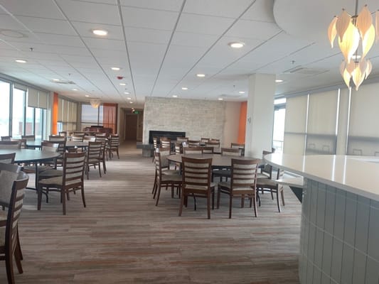 A spacious dining room with round tables and chairs, featuring a stone fireplace.