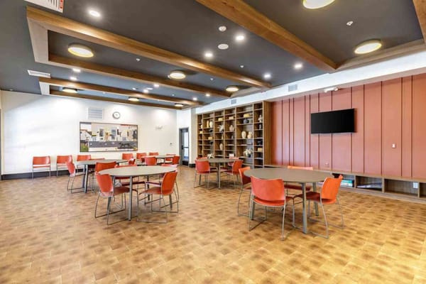 Bright common area with tables and orange chairs in The Meadowmark facility
