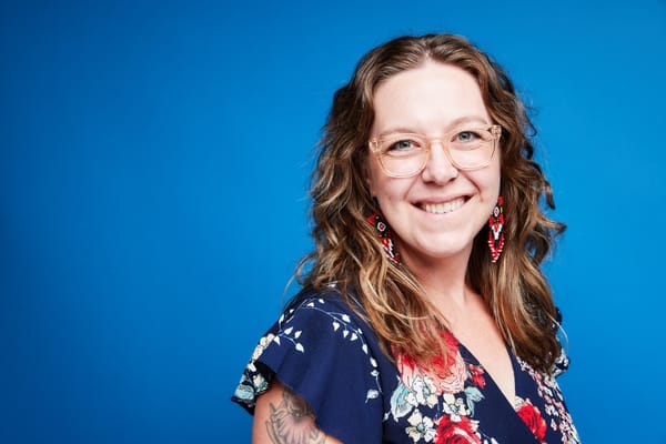 Close-up portrait of a smiling staff member with curly hair and glasses