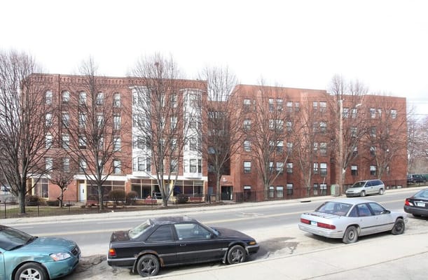 Exterior view of a senior living facility with trees and parked cars