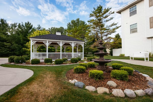 White gazebo with a fountain in a landscaped garden