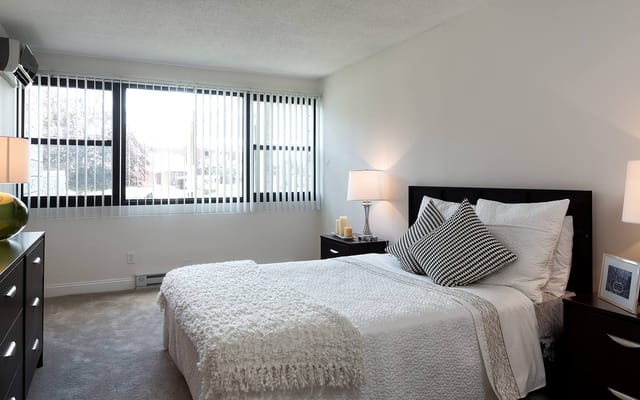 A cozy bedroom with a bed, bedside lamps, and large windows