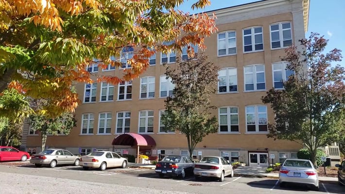View of River Park Apartments featuring trees and parked cars.