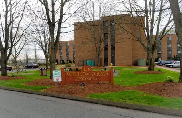 Exterior view of Willow Arms Apartments with a sign.
