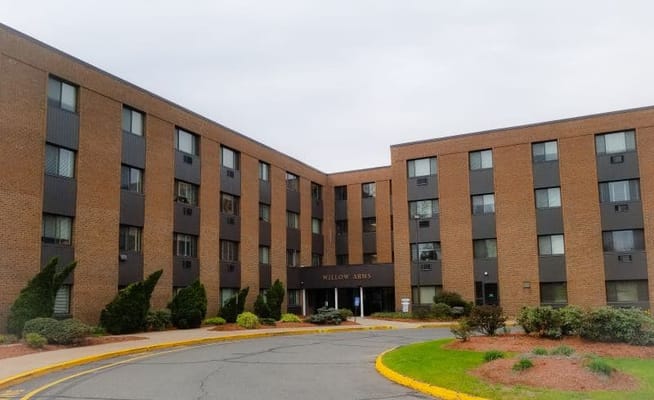 Front view of Willow Arms Apartments showing the entrance and surrounding landscape.