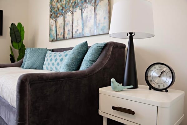 A cozy living room with a grey couch, decorative pillows, a lamp, and a clock.