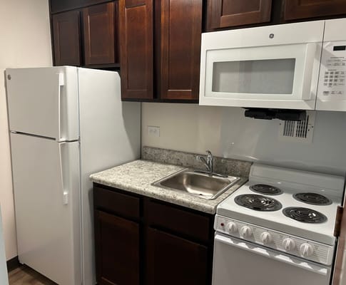 Small kitchen area featuring a refrigerator, sink, stove, and microwave.